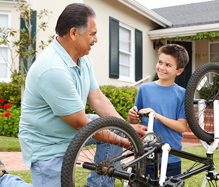 Grandfather kneeling beside his grandson helping him fix a bicycle on the front lawn