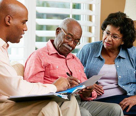 Senior adult couple sitting down on a couch in their living room going over paperwork with a business professional